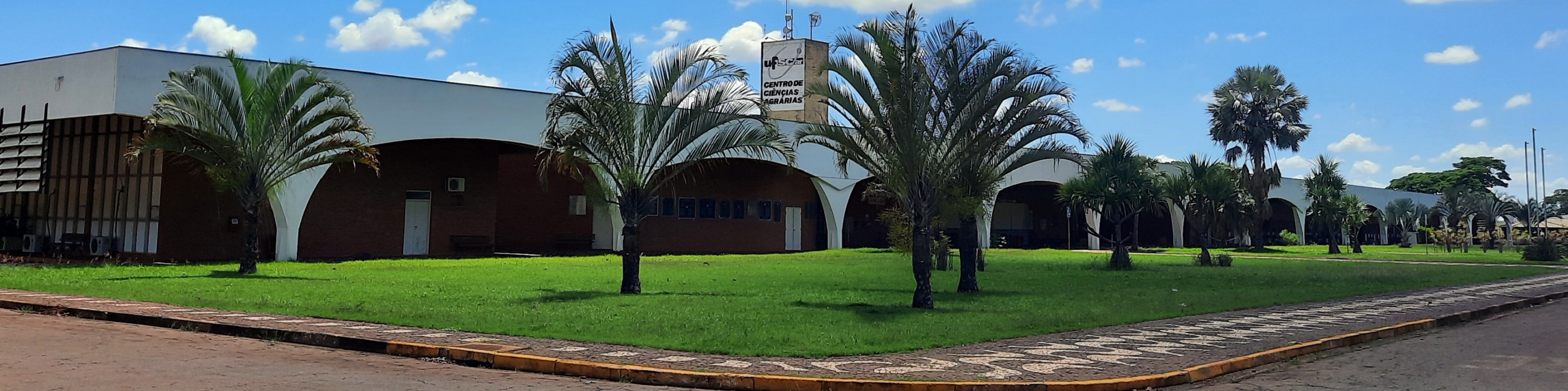 Visão frontal do Prédio Central do Centro de Ciências Agrárias (CCA), UFSCar, campus Araras. Céu, árvores, gramado e calçada
